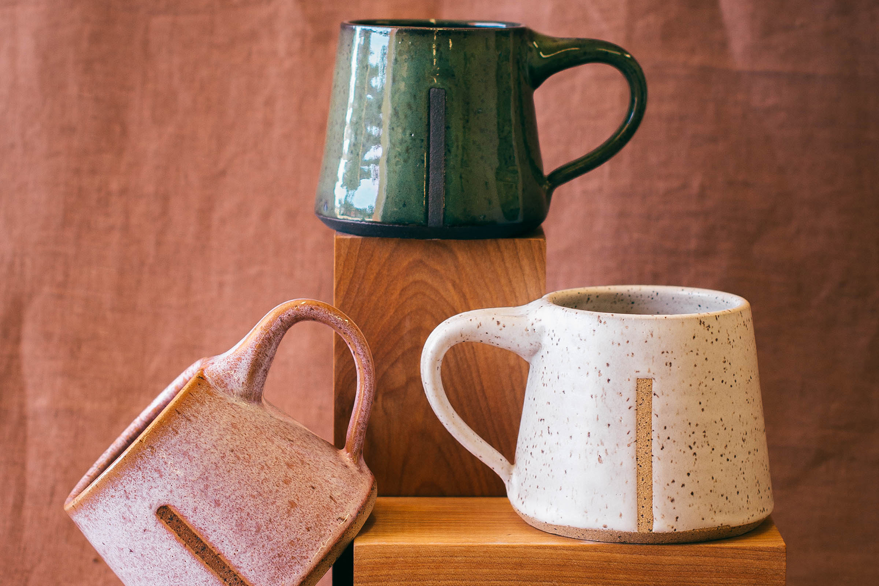 Three glazed, ceramic mugs with an angular shape.